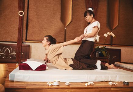 Thai masseuse sitting on woman and pulling her arms